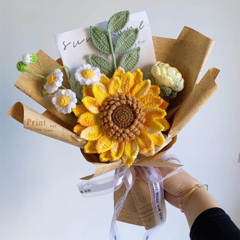 Gehaakt bloemenboeket met zonnebloem, madeliefjes en bladeren in kraftpapieren kegel