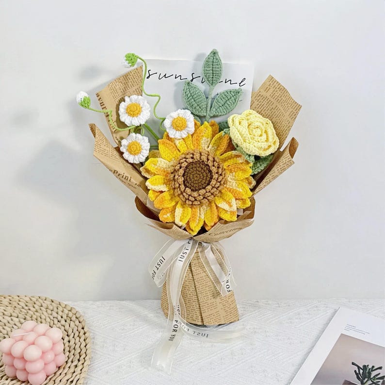 Gehaakt bloemenboeket met zonnebloem, madeliefjes en bladeren in kraftpapieren kegel